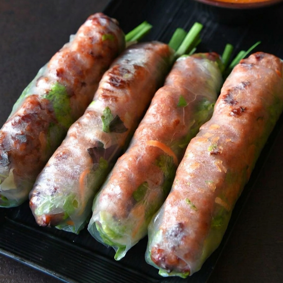 Four fresh Vietnamese spring rolls filled with grilled meat, vegetables, and herbs on a black rectangular plate.